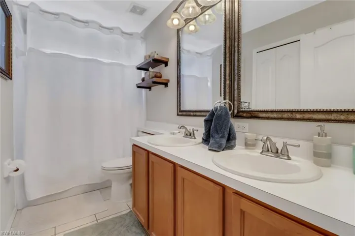 Bathroom with double-sink vanity, toilet, curtained shower, and tile patterned flooring