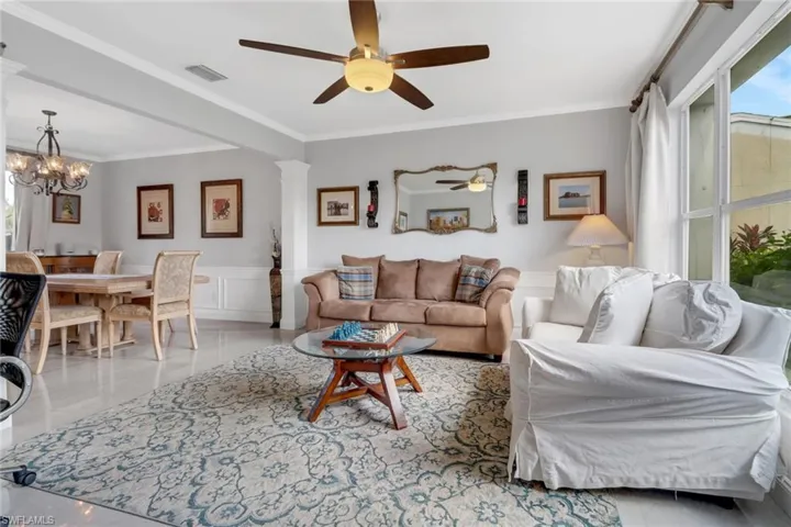 Living room featuring decorative columns, crown molding, ceiling fan, notable chandelier, and light tile patterned floors