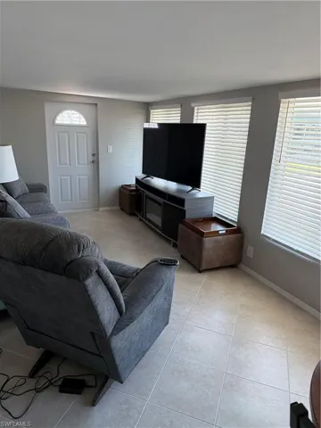 Living area featuring light-toned tile flooring, light gray walls, and several windows with blinds