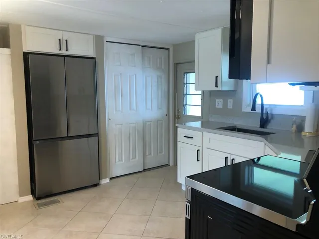Kitchen featuring stainless steel appliances refrigerator, sink, and white cabinets