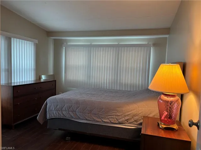 Bedroom featuring dark wood flooring and ample natural light from two windows with vertical blinds