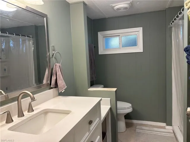 Bathroom with a white vanity featuring a rectangular sink and brushed nickel faucet, a large mirror, and a window providing natural light