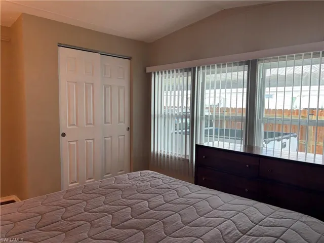 This room features a vaulted ceiling, a closet with sliding panel doors, and windows with vertical blinds