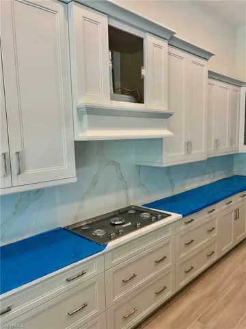 Kitchen featuring white cabinetry, light hardwood / wood-style flooring, tasteful backsplash, and black electric stovetop