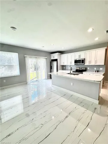 Kitchen featuring stainless steel appliances, recessed lighting, light countertops, a center island with sink, and white cabinetry