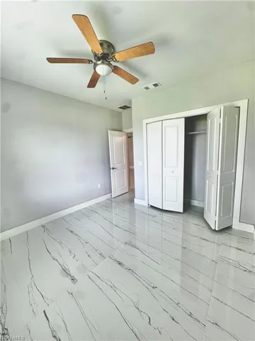 Unfurnished bedroom with marble look tile flooring, a closet, and ceiling fan