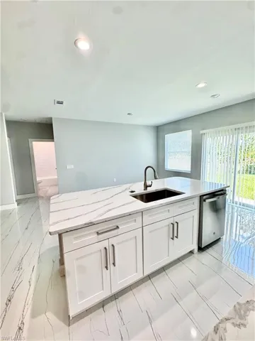 Kitchen featuring dishwasher, white cabinets, recessed lighting, light marble finish flooring, and light stone countertops