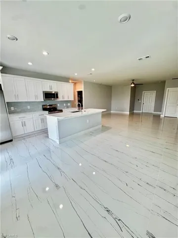 Kitchen with stainless steel appliances, light marble finish flooring, white cabinets, decorative backsplash, and light countertops