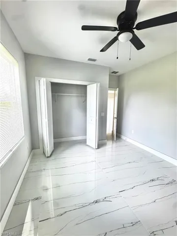 Unfurnished bedroom featuring light marble finish floors, a closet, and a ceiling fan