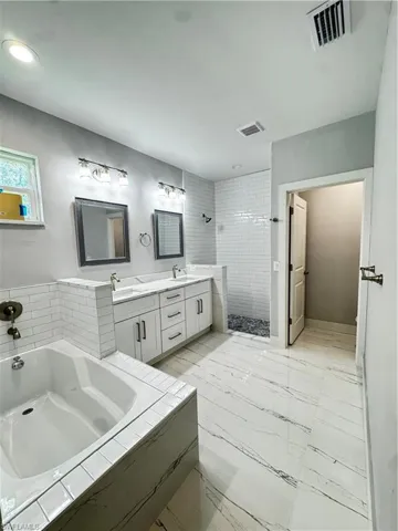 Full bath with a stall shower, double vanity, a garden tub, and marble finish flooring