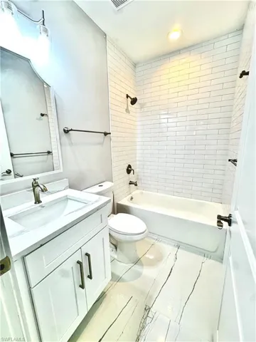 Full bath featuring vanity, tub / shower combination, marble look tiles, and recessed lighting