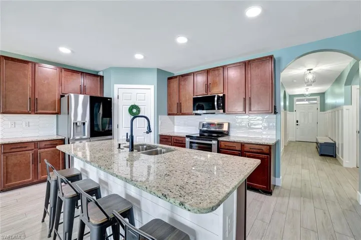 Kitchen featuring appliances with stainless steel finishes, a breakfast bar area, light stone countertops, arched walkways, and wainscoting