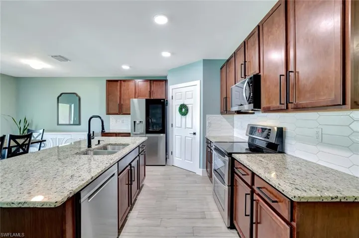 Kitchen featuring appliances with stainless steel finishes, light wood finished floors, light stone counters, decorative backsplash, and recessed lighting