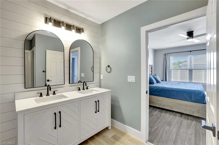 Full bath with ensuite bath, wood finished floors, double vanity, a ceiling fan, and wood walls