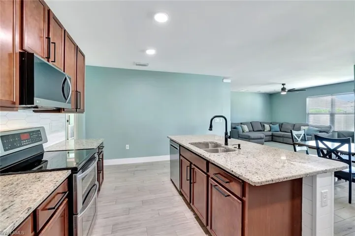 Kitchen featuring appliances with stainless steel finishes, a ceiling fan, light stone counters, an island with sink, and open floor plan