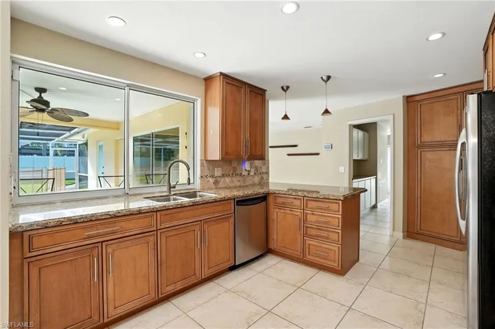 Kitchen with brown cabinetry, light stone counters, stainless steel appliances, ceiling fan, and pendant lighting