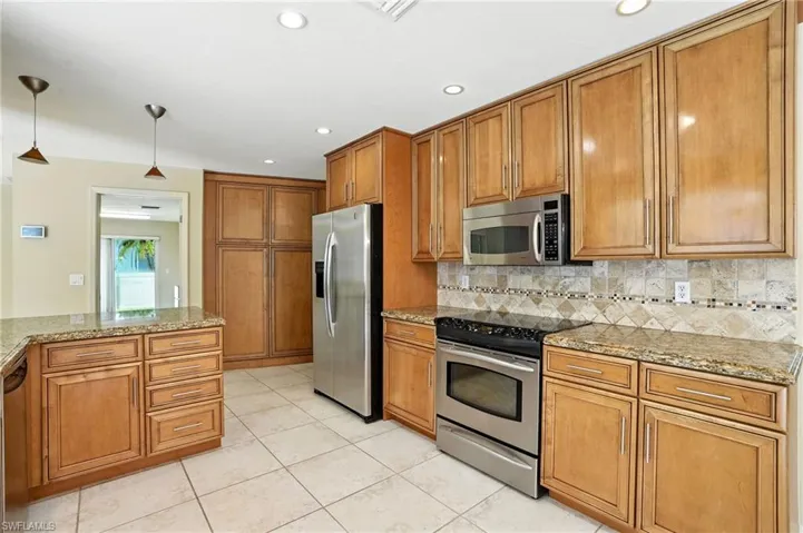 Kitchen with brown cabinets, appliances with stainless steel finishes, decorative light fixtures, light stone countertops, and recessed lighting