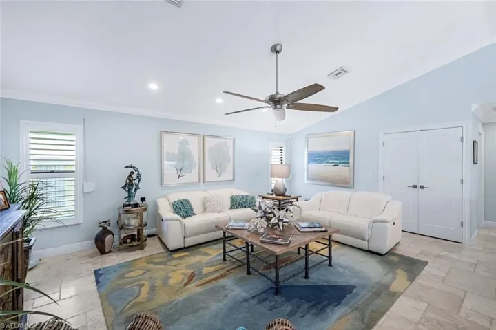 Living room featuring crown molding, vaulted ceiling, plantation shutters & ceiling fan.
