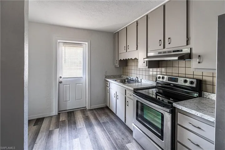 Kitchen with electric stove, sink, hardwood / wood-style floors, and backsplash
