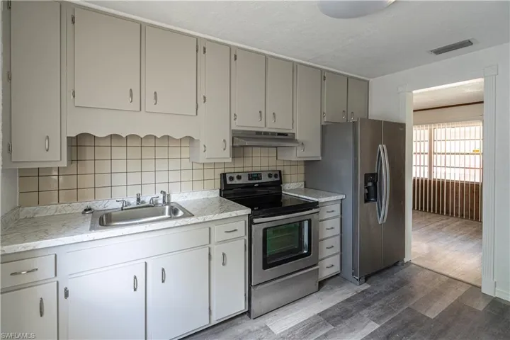 Kitchen with stainless steel appliances, wood-type flooring, gray cabinets, backsplash, and sink