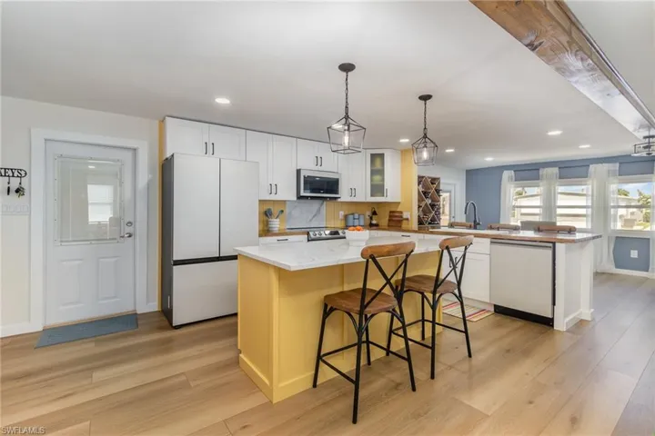 Kitchen featuring freestanding refrigerator, a peninsula, light wood-type flooring, dishwashing machine, and white cabinetry
