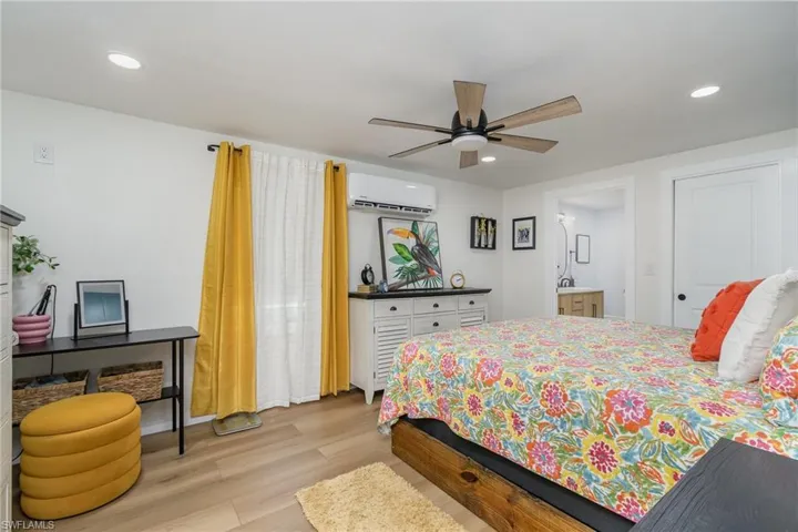 Bedroom with light wood finished floors, recessed lighting, an AC wall unit, ensuite bath, and ceiling fan
