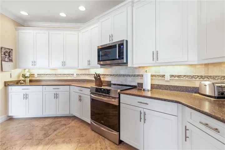 Kitchen featuring white cabinetry, ornamental molding, appliances with stainless steel finishes, and tasteful backsplash