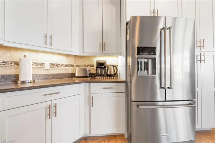 Kitchen featuring high end refrigerator, backsplash, white cabinetry, and dark stone countertops