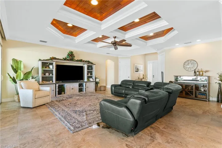 Living room with beam ceiling, ceiling fan, wooden ceiling, coffered ceiling, and crown molding