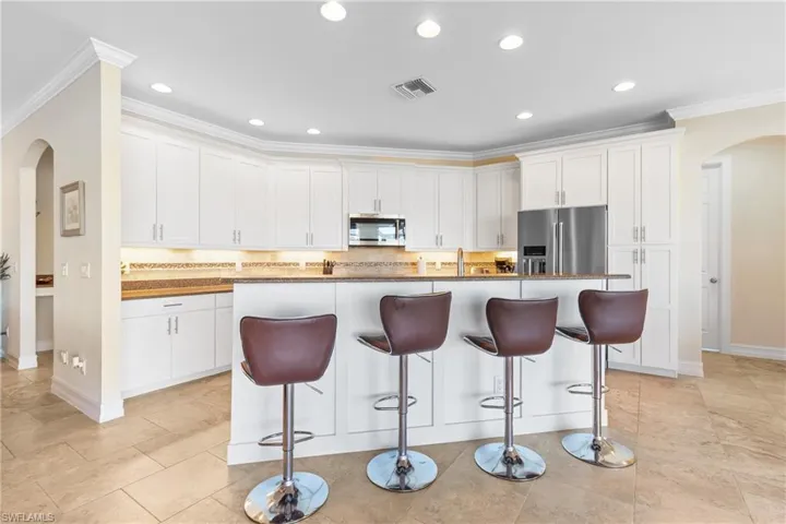 Kitchen featuring stainless steel appliances, white cabinetry, a kitchen island with sink, and crown molding