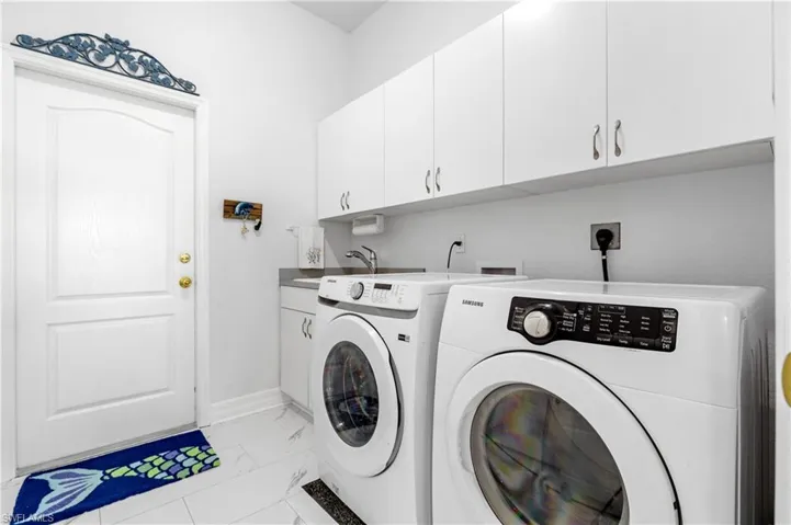 Clothes washing area with baseboards, marble finish floor, a sink, cabinet space, and separate washer and dryer