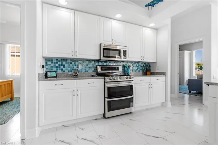 Kitchen with tasteful backsplash, stainless steel appliances, baseboards, marble finish floor, and white cabinets