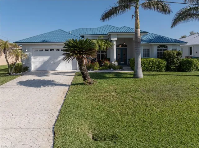 View of front of property featuring driveway, metal roof, an attached garage, and a front yard