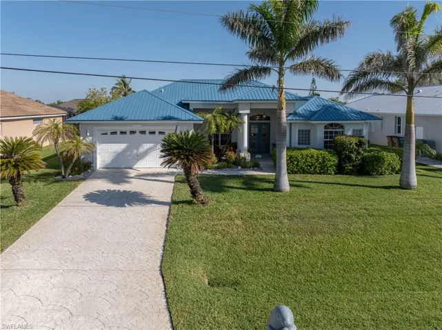 Single story home with metal roof, an attached garage, concrete driveway, a front yard, and french doors