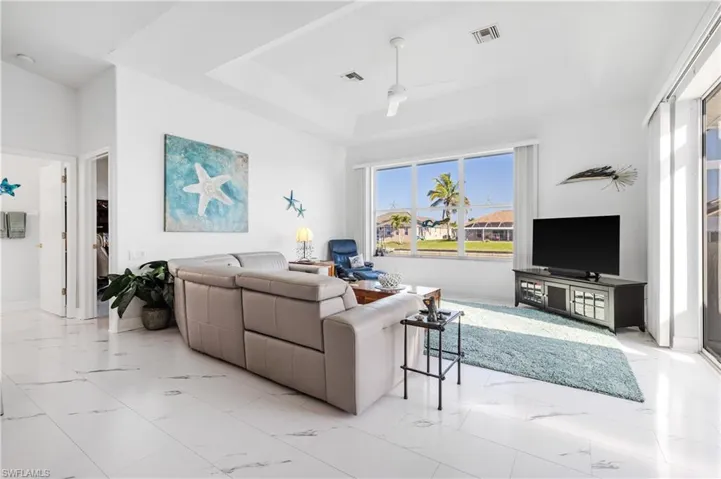 Living room featuring marble finish floor, a raised ceiling, a ceiling fan, and visible vents