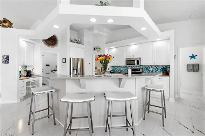 Kitchen featuring a ceiling fan, tasteful backsplash, stainless steel appliances, marble finish floor, and white cabinets