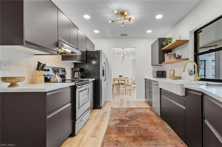 Kitchen featuring appliances with stainless steel finishes, a chandelier, light wood-style flooring, dark cabinetry, and under cabinet range hood