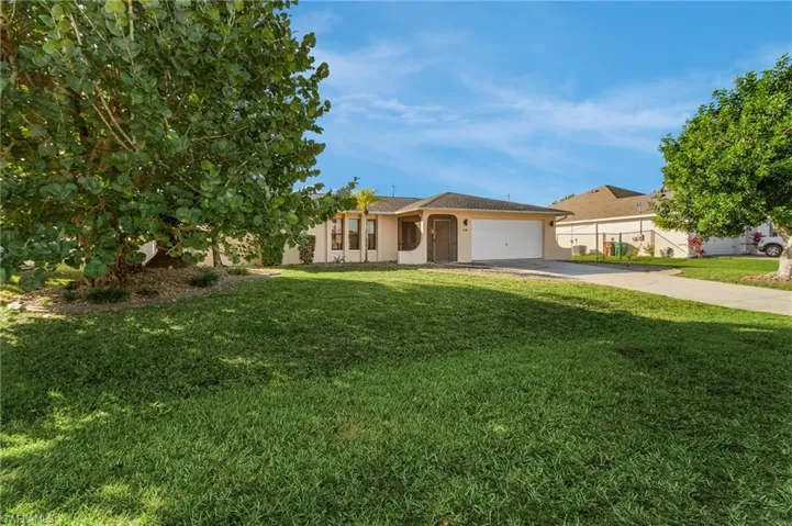 Ranch-style home featuring driveway, a front lawn, an attached garage, and stucco siding