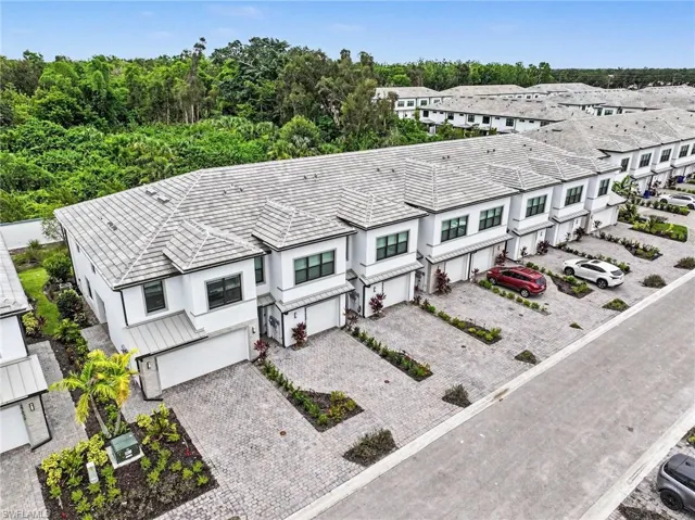 Modern townhome row featuring white exteriors with gray trim, individual attached garages, paver driveways, and landscaped front entries