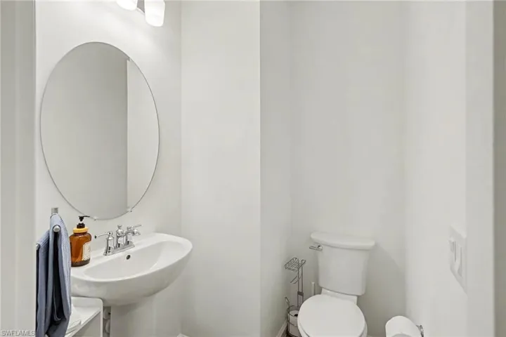 Pedestal sink with chrome faucet, oval mirror, and wall-mounted vanity lighting