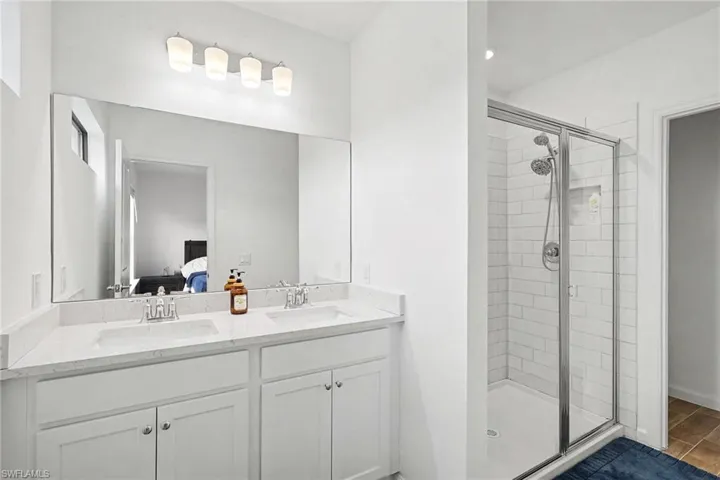 Bathroom featuring a dual vanity with white cabinetry, light-toned countertops, and a full-width mirror