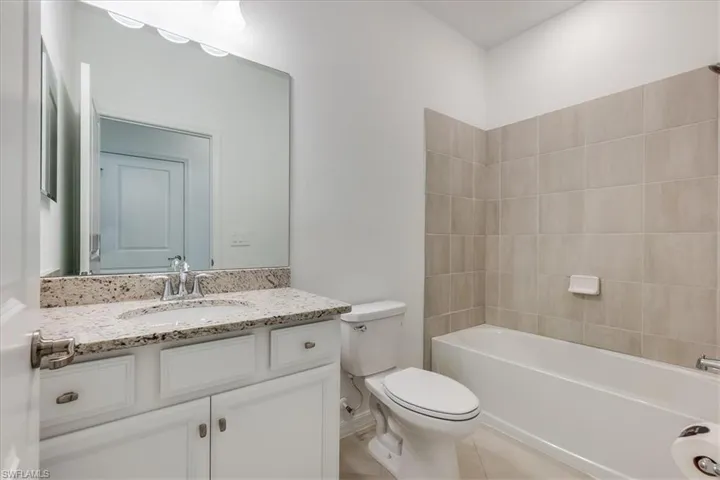 Full bathroom featuring tiled shower/bath, tile flooring, toilet, and large vanity.