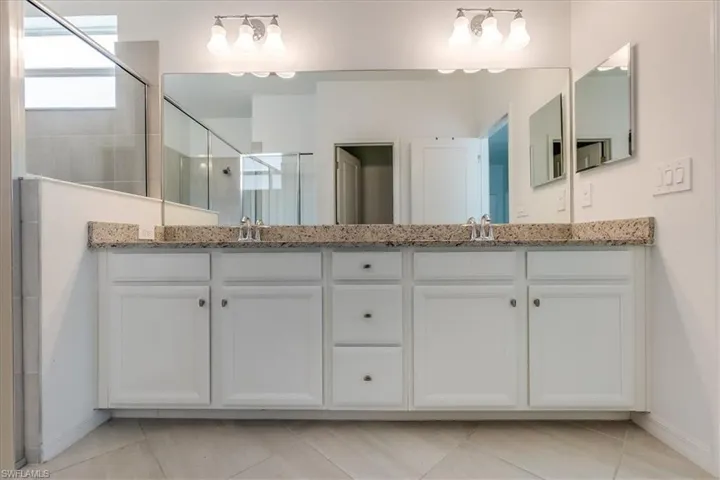 Primary bathroom featuring tile floors, an enclosed shower, double sink, and vanity with extensive cabinet space