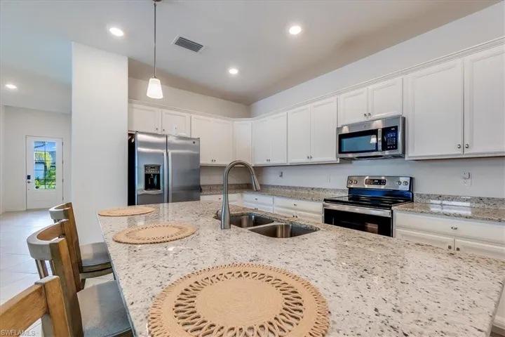 Kitchen featuring decorative light fixtures, sink, white cabinetry, and stainless steel appliances.