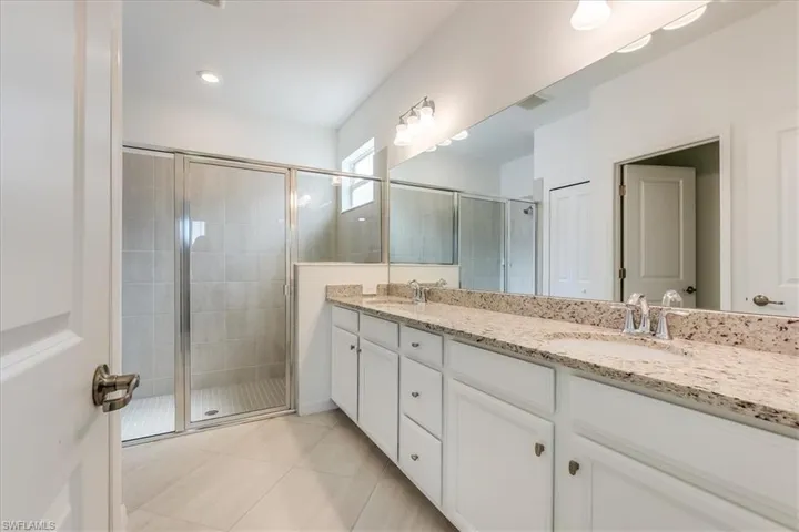 Primary bathroom featuring double vanity, tile flooring, and a shower with shower door