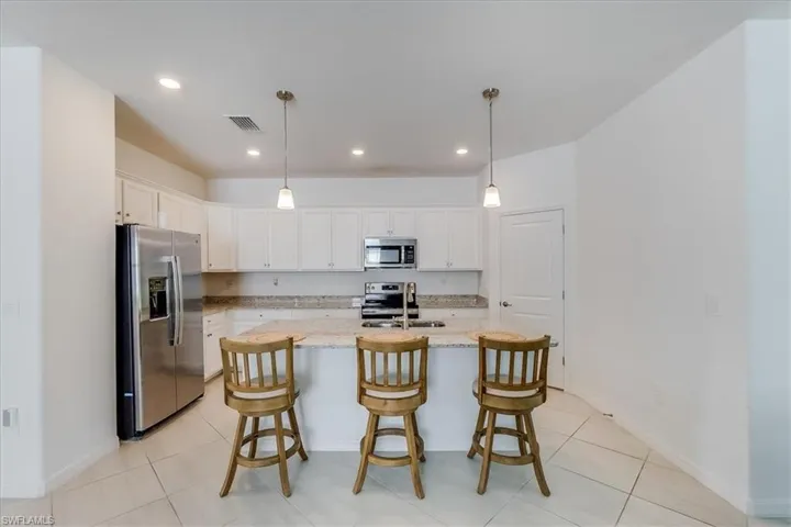Kitchen featuring stainless steel appliances, light stone counters and a kitchen island with sink.