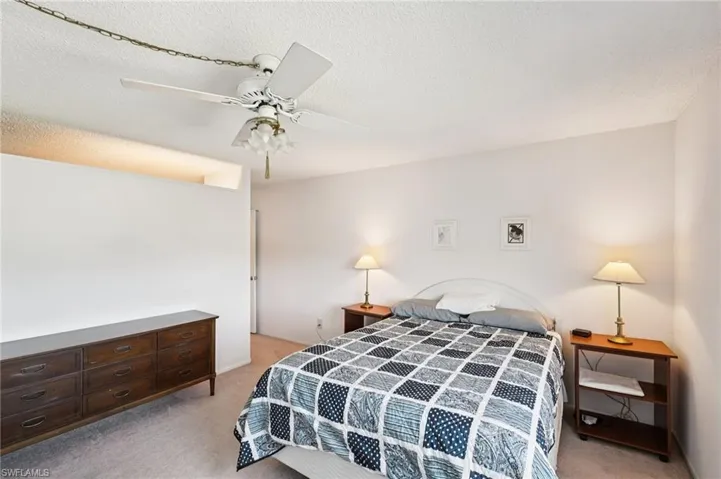 Bedroom with light colored carpet, a textured ceiling, and ceiling fan