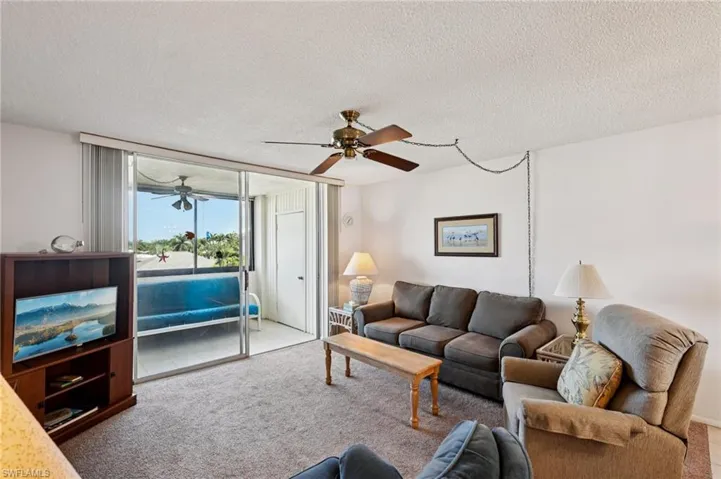 Carpeted living room with a textured ceiling, a ceiling fan, and expansive windows