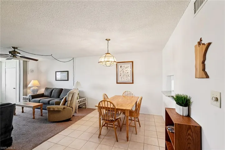 Dining room with light tile patterned floors, a ceiling fan, a textured ceiling, light colored carpet, and suspended lighting