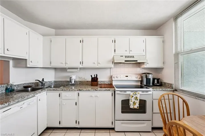 Kitchen with white appliances, white cabinets, light tile patterned floors, and tasteful backsplash